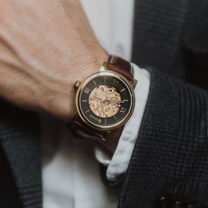 Close-up of a person wearing a luxurious watch with a brown leather strap and gold detailing.