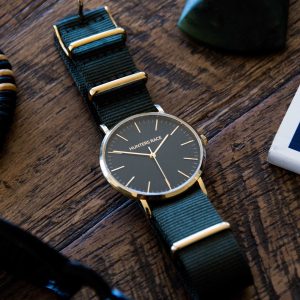 Watch with green strap and gold accents on a wooden surface
