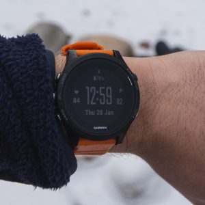 Garmin smartwatch on a wrist with an orange band, blurred snowy background