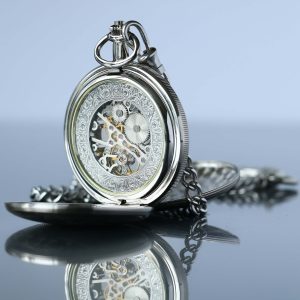 Silver pocket watch with intricate mechanical design on a reflective surface