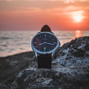 Wristwatch on a rock with a sunset over water in the background