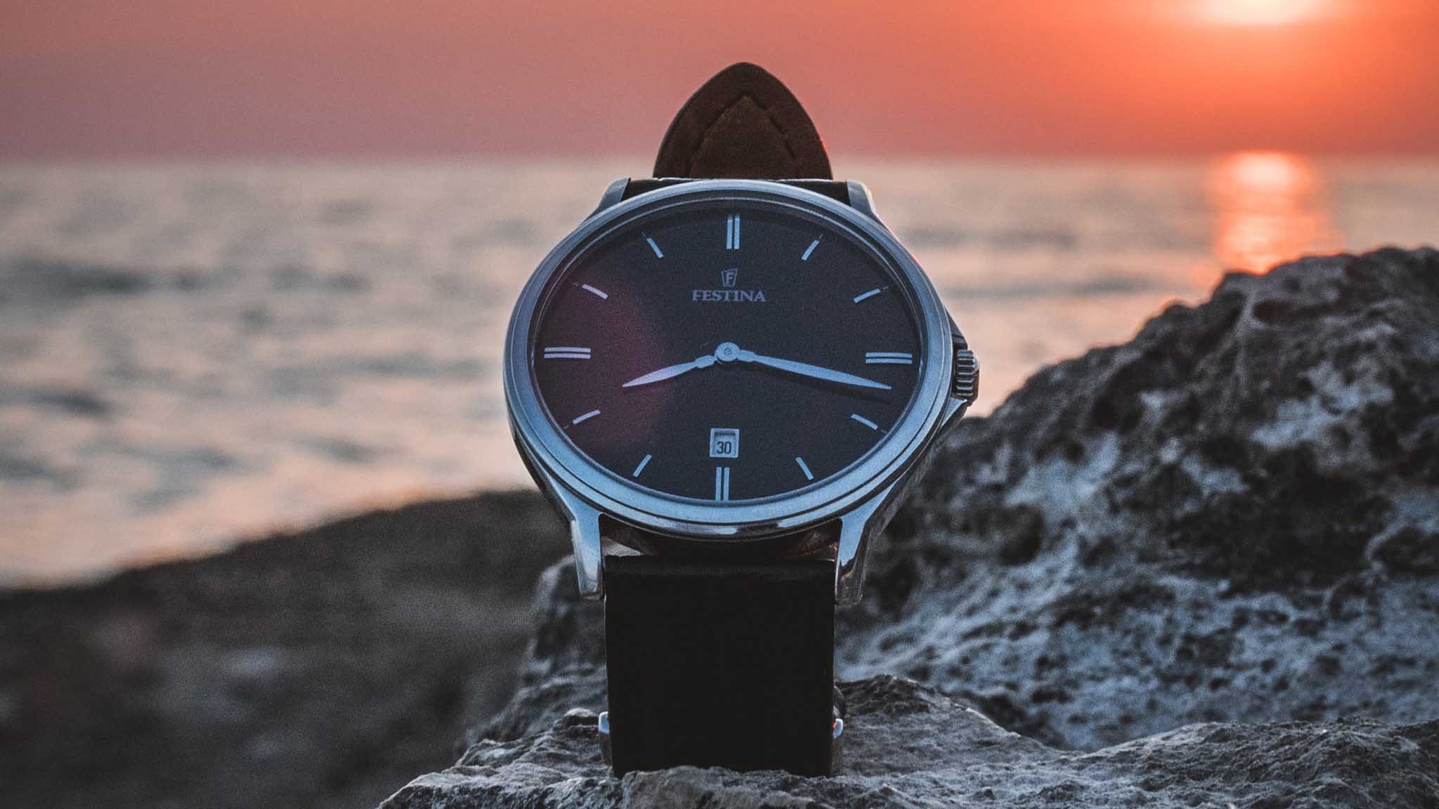 Wristwatch on a rock with a sunset over water in the background